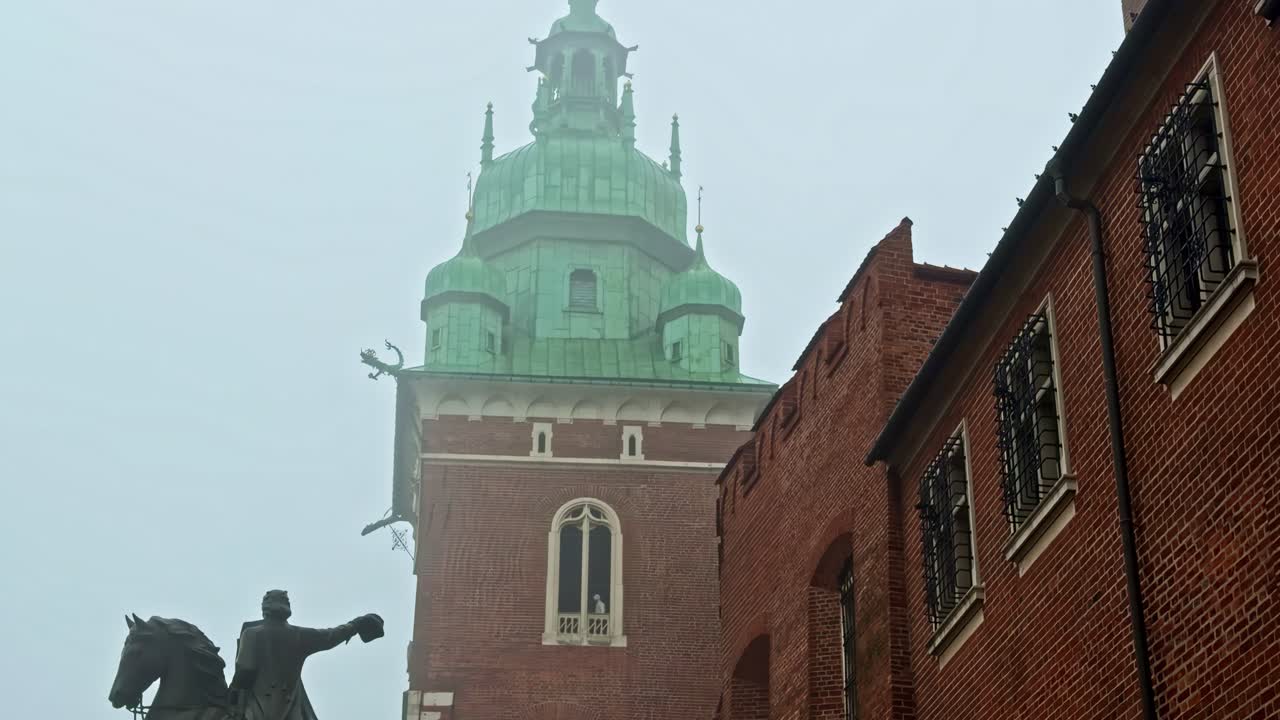 Vista nebbiosa della torre del Castello Reale di Wawel e della statua equestre a Cracovia, Polonia, con nuvole drammatiche: paesaggio urbano invernale suggestivo per viaggi e uso editoriale