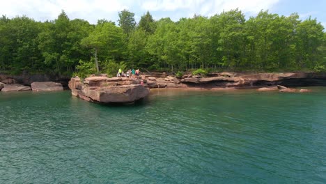 la gente salta del acantilado de una roca al lago superior en un día de verano, se divierte en la isla de madeline, la isla del apóstol, el lago superior de wisconsin, viaja y disfruta del aire libre