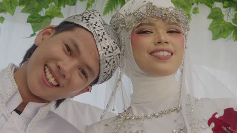 low angle view of asian bride and groom in traditional sundanese wedding outfit looking at camera smiling