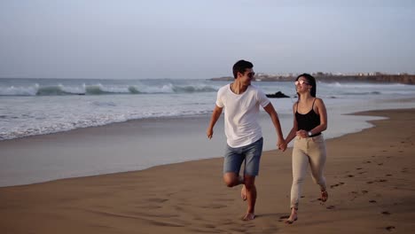 Ein-Paar-Genießt-Den-Sommerurlaub-Am-Großen-Strand,-Genießt-Das-Leben-Und-Läuft-In-Zeitlupenvideo-über-Die-Meereslandschaft-Im-Hintergrund.-Junges-Paar-Rennt-In-Den-Tropischen-Ozean,-Glückliches-Lächeln