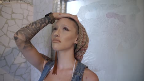 a young woman with alternative clothing and tattoos is leaning towards a mosaic wall looking hopeless, nervous and stressed