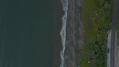 top-down shot of dark blue sea with waves splashing on the sandy shore in the philippines - aerial drone shot