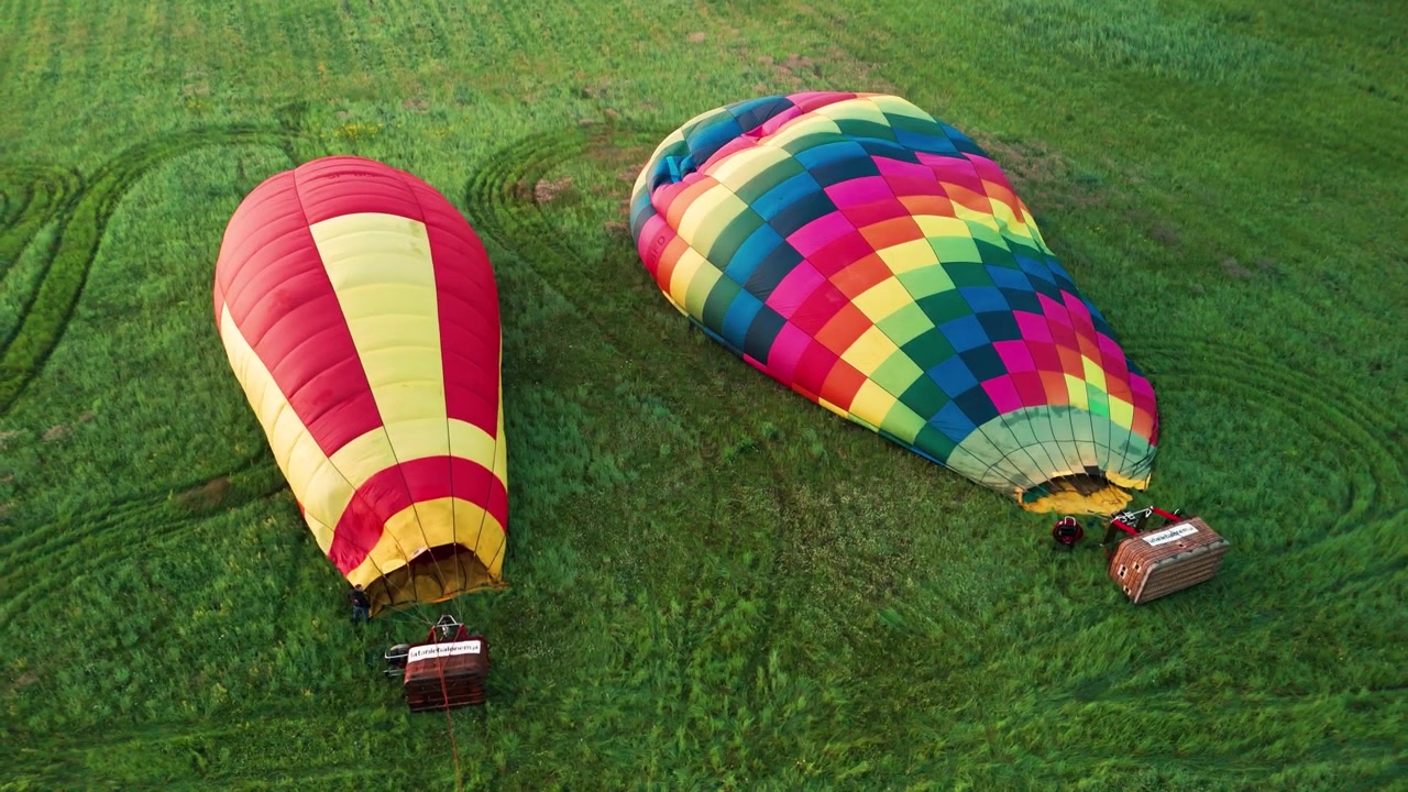 Cinematic high angle of colorful hot air balloons being prepared for flight in a lush meadow during golden hour. Perfect for travel and adventure content.
