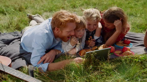 Family-watching-tablet-computer-on-picnic-lying-green-grass.-Summer-vacation.