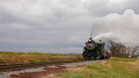 un ángulo bajo de un tren de vapor soplando a lo largo de una vía férrea en un día ventoso