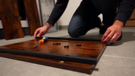 close-up of male hands assembling wooden furniture with screwdriver on floor