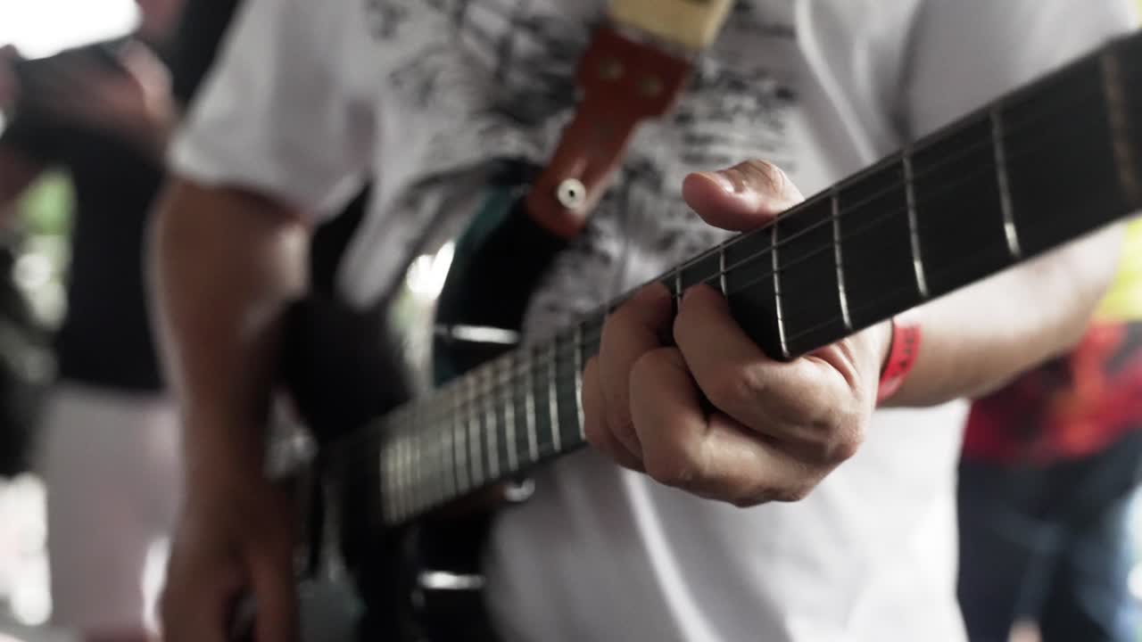 Hænderne på en mandlig musiker med hvid skjorte, der spiller elektrisk guitar i slow motion