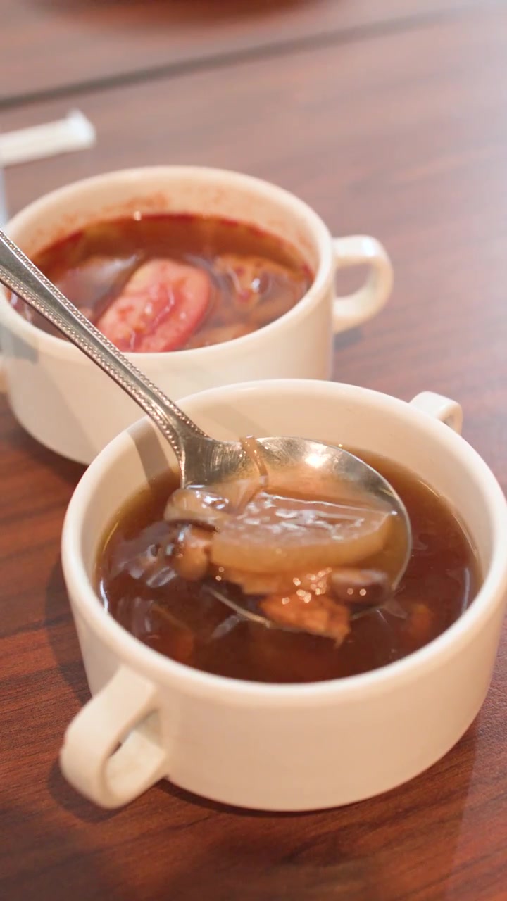 木製のテーブルの上で、湯気の立つキノコ入り茶色いスープを金属のスプーンでかき混ぜるクローズアップ