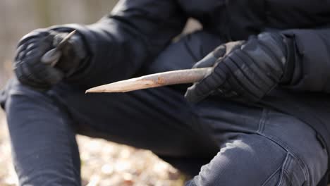 hombre usando un cuchillo para afilar la rama del árbol preparando el campamento en el bosque en el frío día de otoño