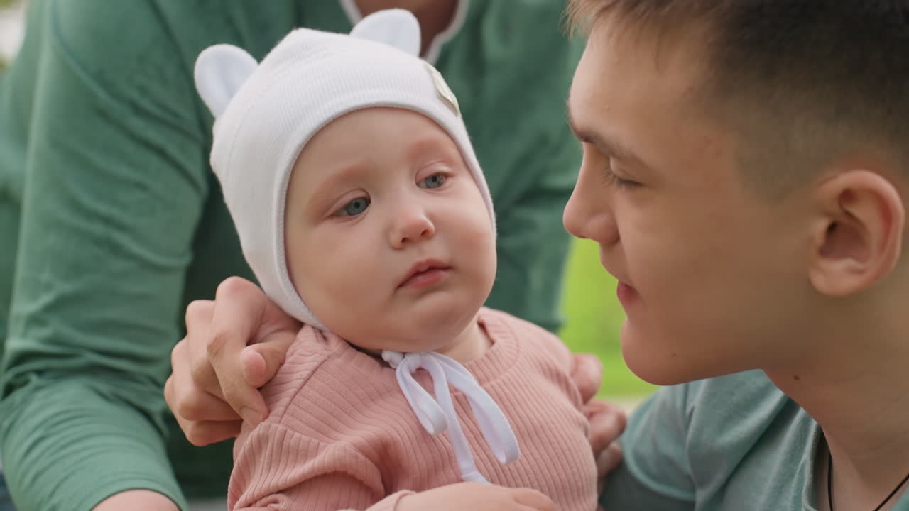 Mother And Father Expressing Affection In Park, Intimate Family Scene In Peaceful Outdoor Spring Setting, Gentle Parental Gesture Showcasing Care And Warmth In Tranquil Park Environment