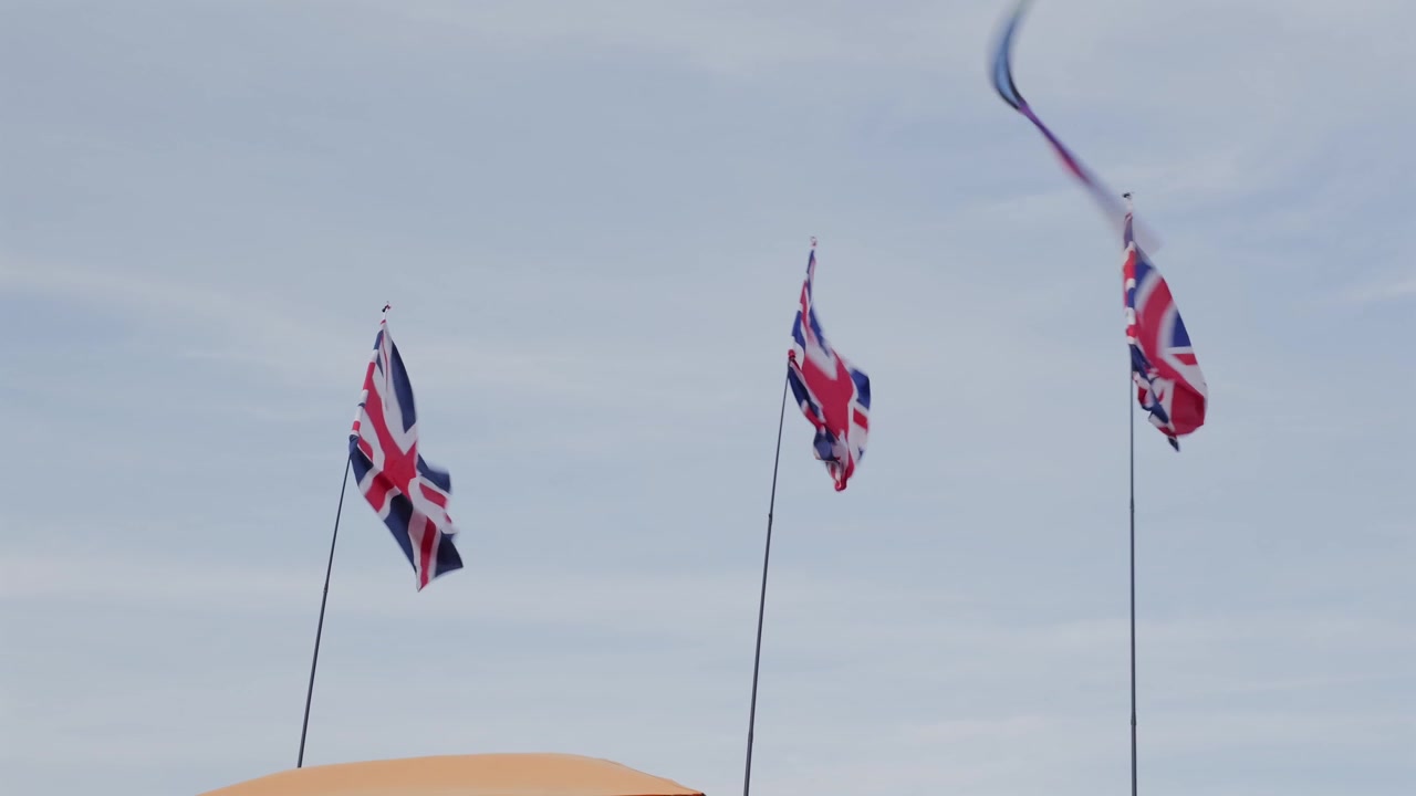 Handheld low angle shot of Union Jack flags waving in cloudy sky