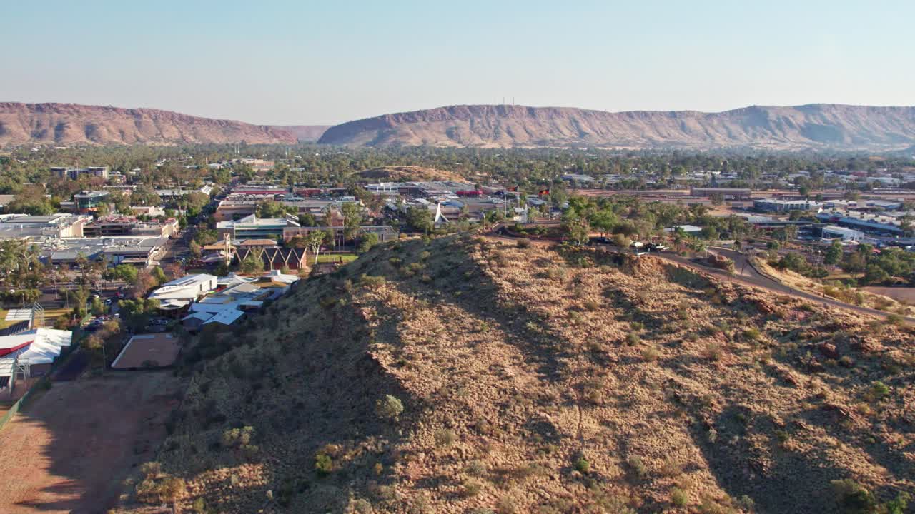Aerial footage moving forwards of Anzac Hill and the town of Alice Springs, Mparntwe, with MacDonnell Ranges in the distance. Northern Territory, Australia. August 2022.