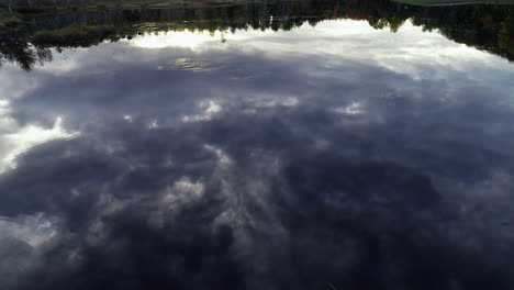 slow moving aerial drone shot over a calm pond with reflections of the clouds in the sky