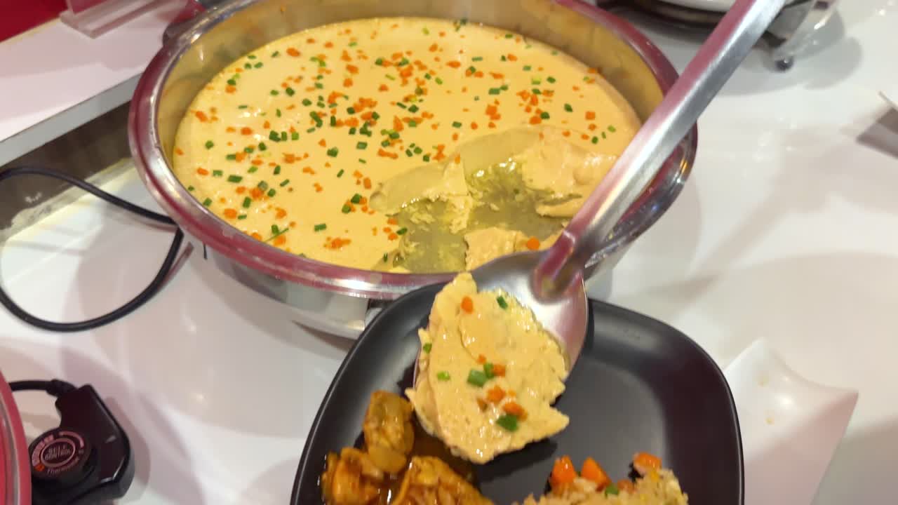 A spoon serves Korean steamed egg onto a plate with rice and chicken in a bright kitchen setting