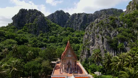 aerial footage from a higher vantage altitude towards this lovely temple revealing mountains, coconut trees and forest, wat khao daeng, khao sam roi yot national park, phrachuap khiri khan, thailand