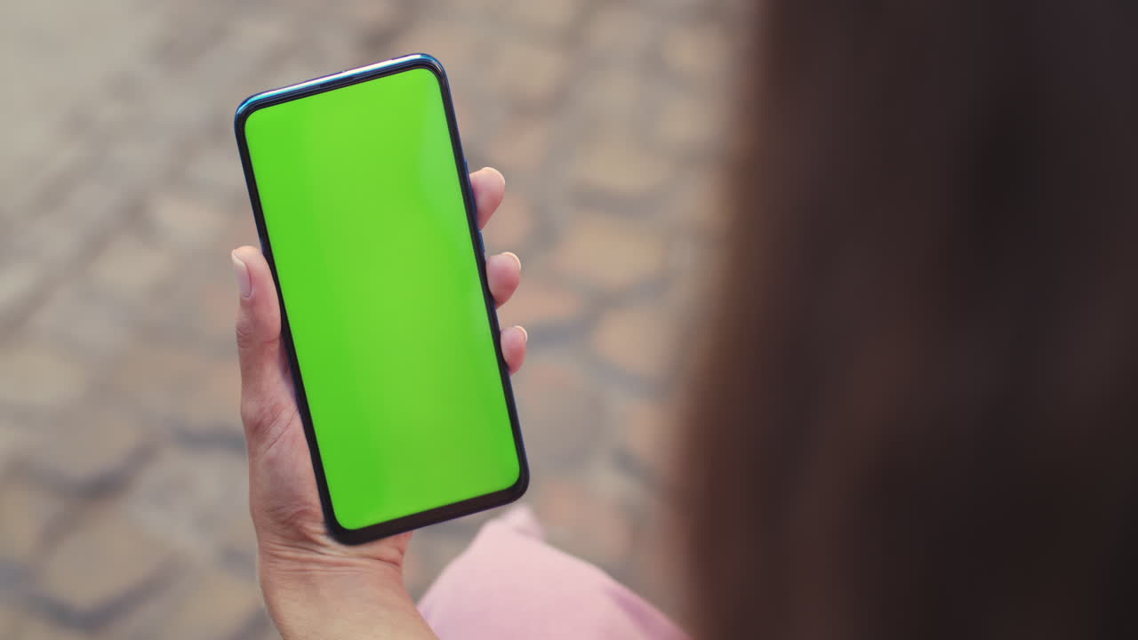 Close-up of a person holding a smartphone with a green screen