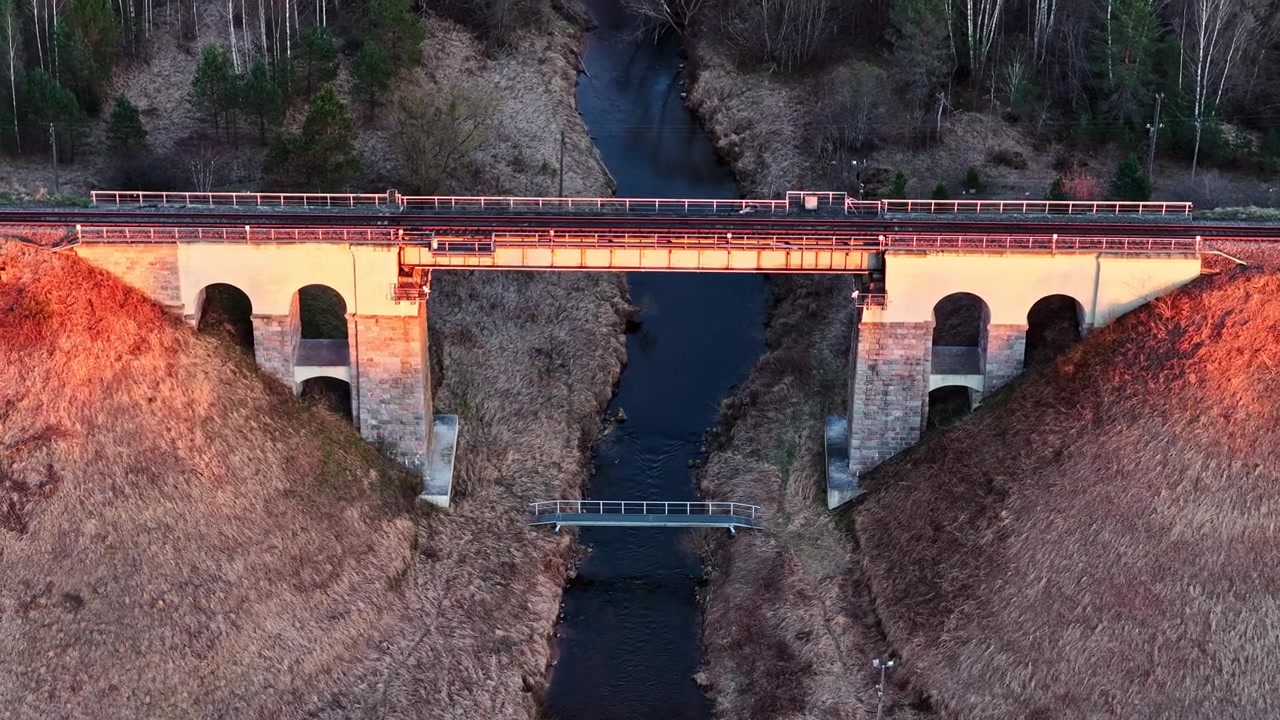 夕暮れの田園風景の中、美しい川に架かる歴史的な石造りのアーチ型鉄道高架橋。