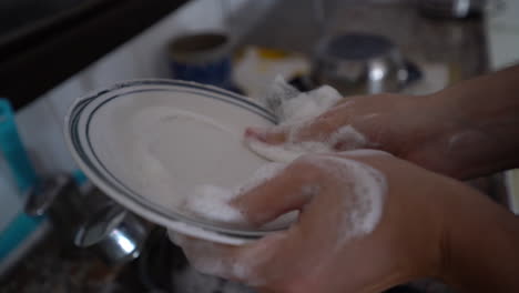 a man is washing a white plate in a sink full of dirty dishes