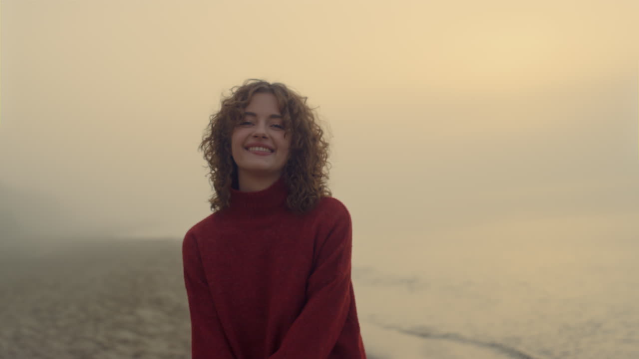 Smiling girl posing at camera. Happy woman posing on sea beach at sunrise