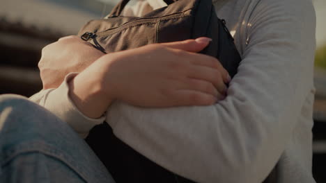 close-up of young woman affectionately holding her bag under warm sunlight, with soft shadows adding depth to her gentle expression, with subtle blur background