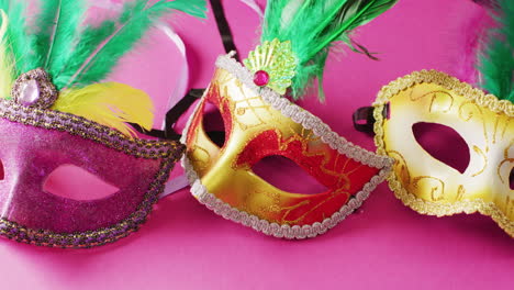 video de tres máscaras de carnaval con plumas verdes sobre un fondo rosado