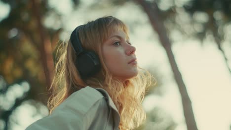 beautiful woman listens to podcast in nature, backlit by sunset, side view