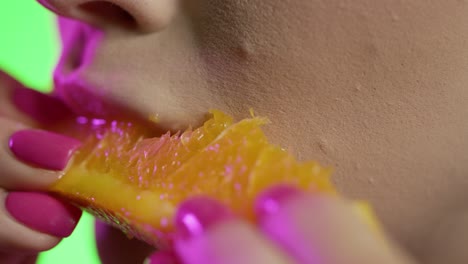 woman biting into a juicy orange slice, green background, neon purple lights