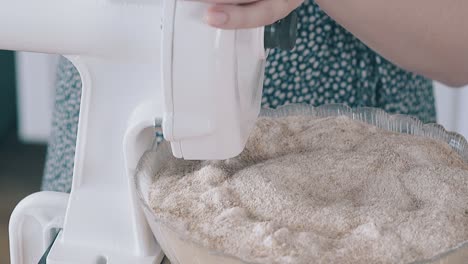 woman-turns-handle-of-domestic-flour-grinder-to-in-kitchen