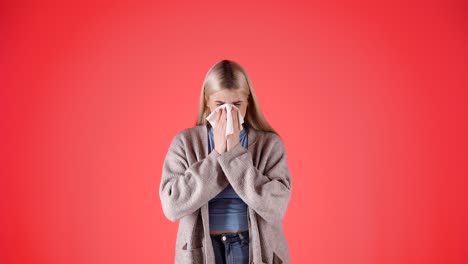 helpless young woman with fever, sneezing in napkin, isolated red background