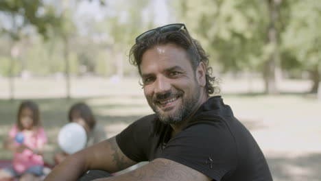 medium shot of smiling man sitting on lawn, looking at camera