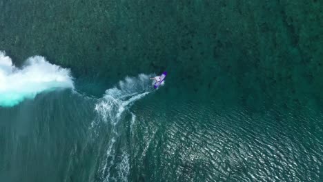 Surfers-catches-wave-in-purple-surfboard-at-a-beach-in-the-Maldives-islands-then-falls-back,-Aerial-top-view-following-shot