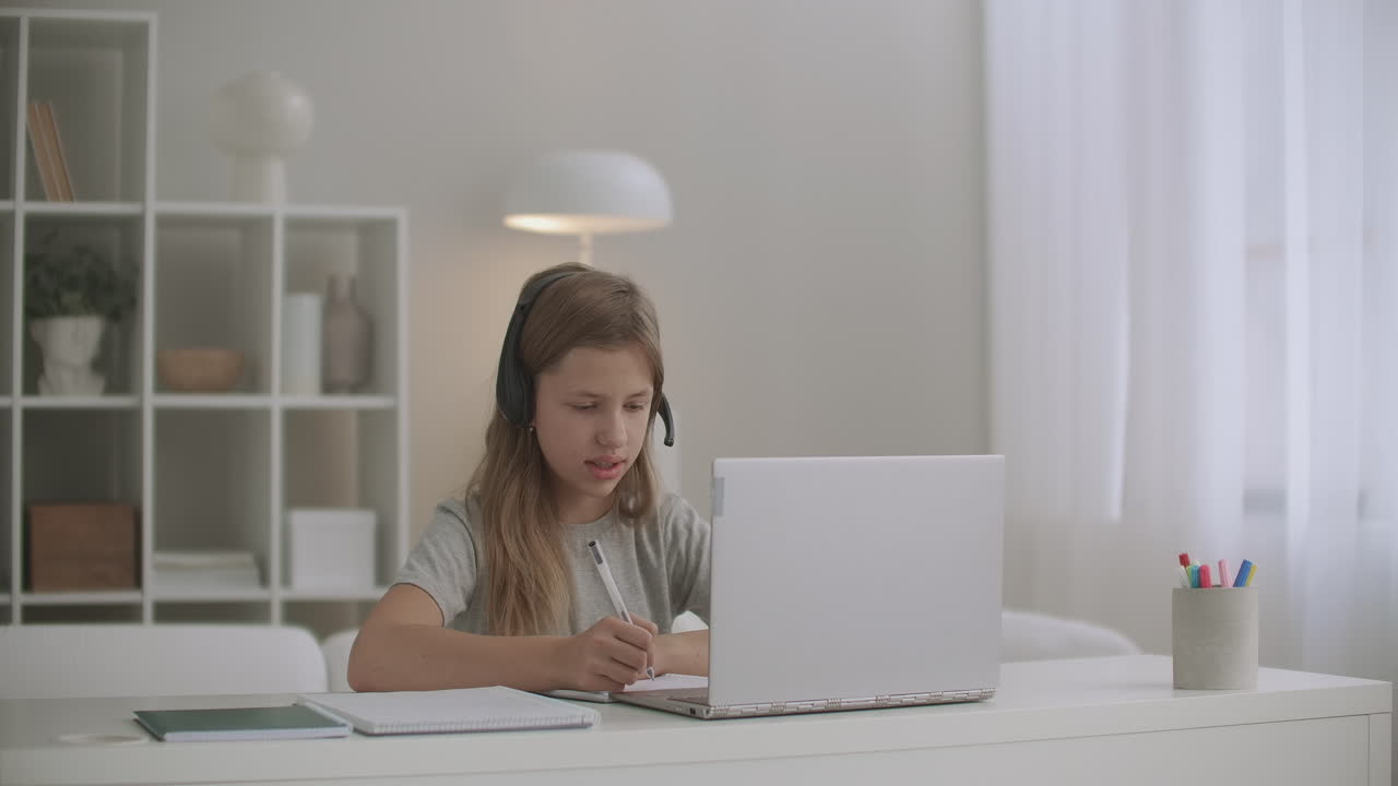 la niña está aprendiendo en línea comunicándose con el maestro por internet usando auriculares y portátil haciendo la tarea en el libro de ejercicios