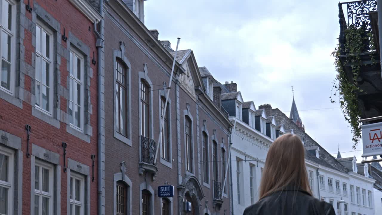 Woman with long blonde hair walking away from the camera down a street in the historic center of Maastricht, Netherlands