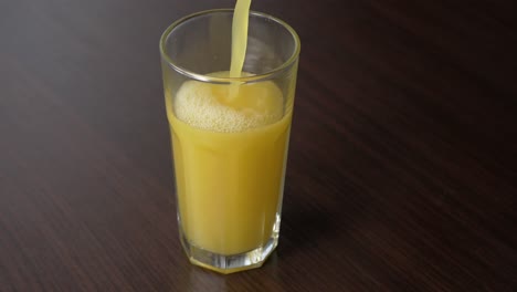 pouring botteled orange juice into a tall glass on a wooden table