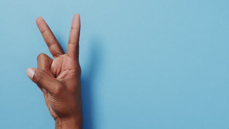 close up of hand of biracial man showing peace sign with copy space on blue background