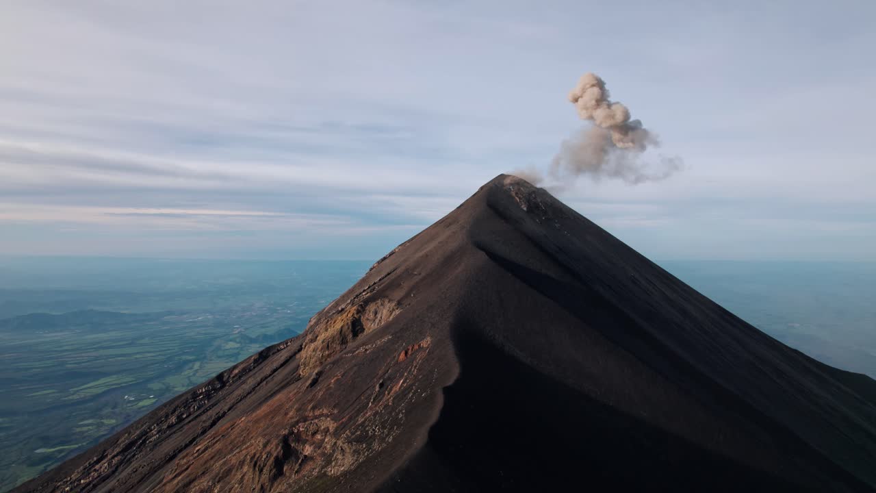 A breathtaking drone shot captures the active Volcán de Fuego in Guatemala, with a plume of ash and gas rising from its summit