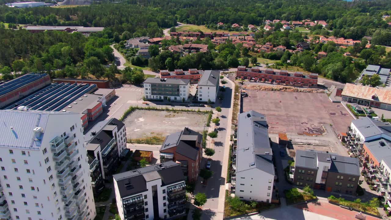 Vista aerea di edifici residenziali misti con tetti rossi, lotto di costruzione e lago in lontananza circondato da alberi verdi a Gustavsberg. Ideale per filmati sull'espansione suburbana.