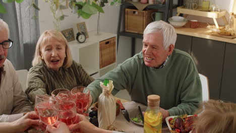 Company-of-Senior-Friends-Clinking-Glasses-at-Home-Dinner