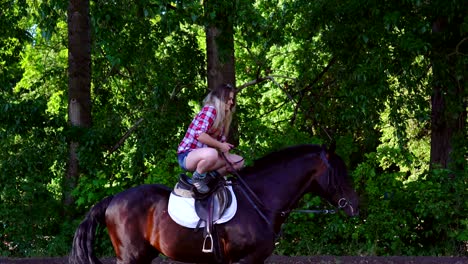 una joven rubia con una camisa a cuadros da un paseo con su caballo. una mujer está de pie en un caballo. noche soleada de verano.