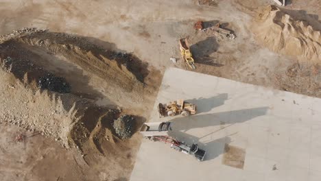 loader and dump truck at work in a construction site on a sunny morning - aerial top-down, static shot