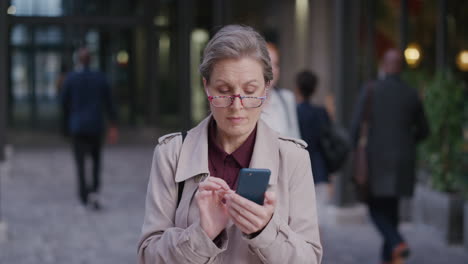 retrato exitoso de una mujer caucásica de mediana edad que usa un teléfono inteligente en la ciudad disfrutando de los mensajes de texto navegando por los mensajes en línea en el teléfono móvil con gafas en cámara lenta