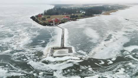 Ventes-horn-lighthouse-in-lithuania-surrounded-by-frozen-water-with-adjacent-rural-landscape,-aerial-view