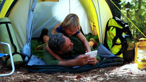 Father-and-son-using-mobile-phone-outside-tent