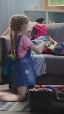 happy mother and daughter gather belongings into suitcase in living room. smiling woman with preschooler girl prepare clothes for dream travel