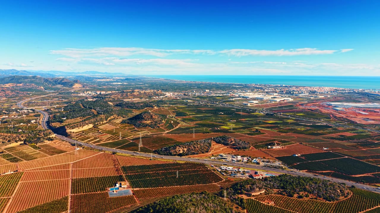 Vista aerea di agrumeti, autostrada e città costiera. Ampia prospettiva di piantagioni di aranci lungo una strada principale che conduce al mare in Spagna.