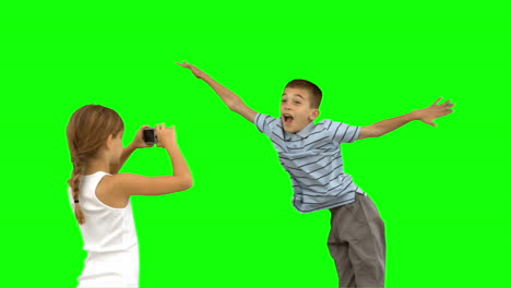 Sister-taking-pictures-of-her-brother-jumping-on-green-screen