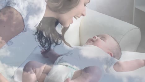 animation of clouds over happy caucasian mother kissing her baby