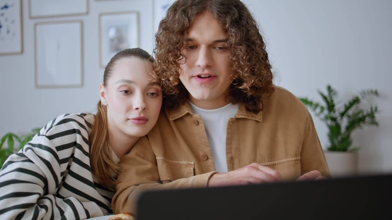 Relaxed spouses watching laptop screen at home breakfast in kitchen closeup
