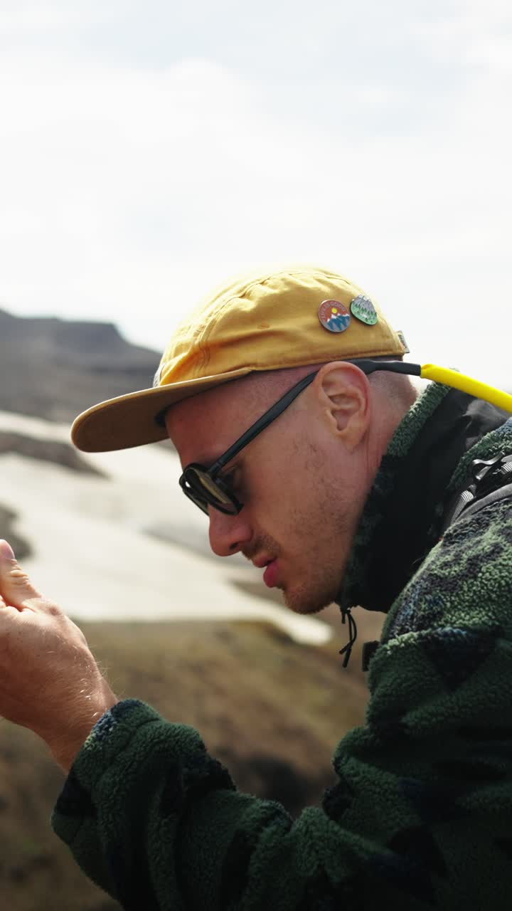 Man in Sunglasses and Cap Examining a Rock Outdoors
