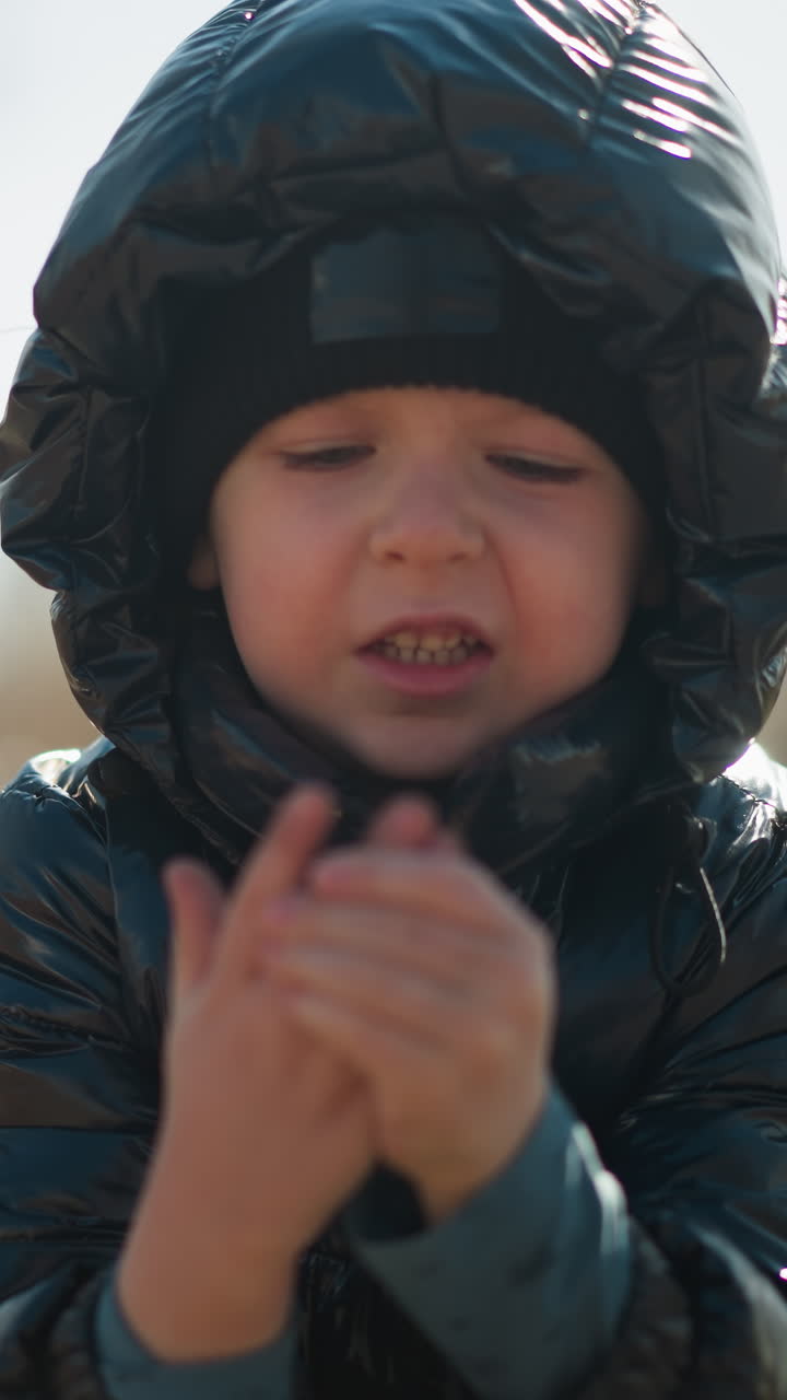 반이는 검은색 재과 헤드 워터를 입은 어린 소년, 그의 입이 약간 열려서 그의 손을 함께 문지르고, 나무와 집의 흐릿한 배경으로